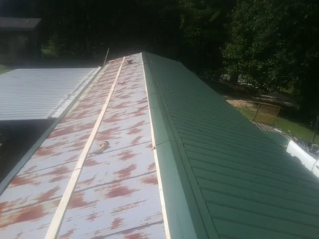 Old rusted panels beside newly installed green metal roofing — Wind Damage Roof Repair by Roofing Brothers in Fredericktown