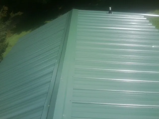 New green metal panels meeting at the ridge of a roof — Flat Roof Repair work by our crew in Fredericktown