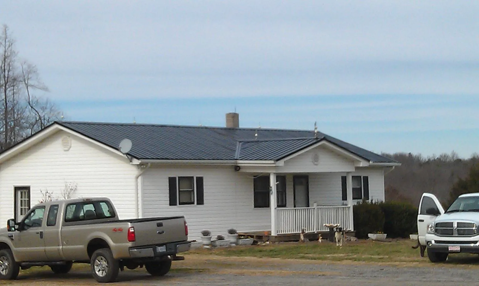 Finished dark metal roof on a white ranch home with work trucks parked in Fredericktown